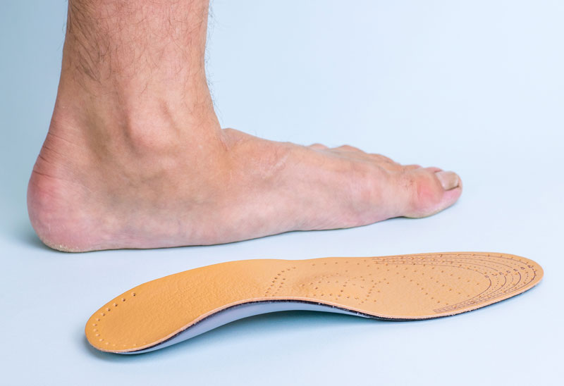 A flat foot is shown planted on the floor, lacking a visible arch. An insole or orthotic device is placed in front of the foot.